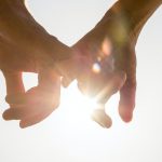 Couple holding hands toward the sun